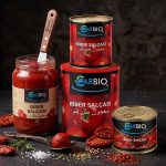 A gourmet food arrangement featuring assorted red peppers, a jar of traditional pepper paste, and tin cans